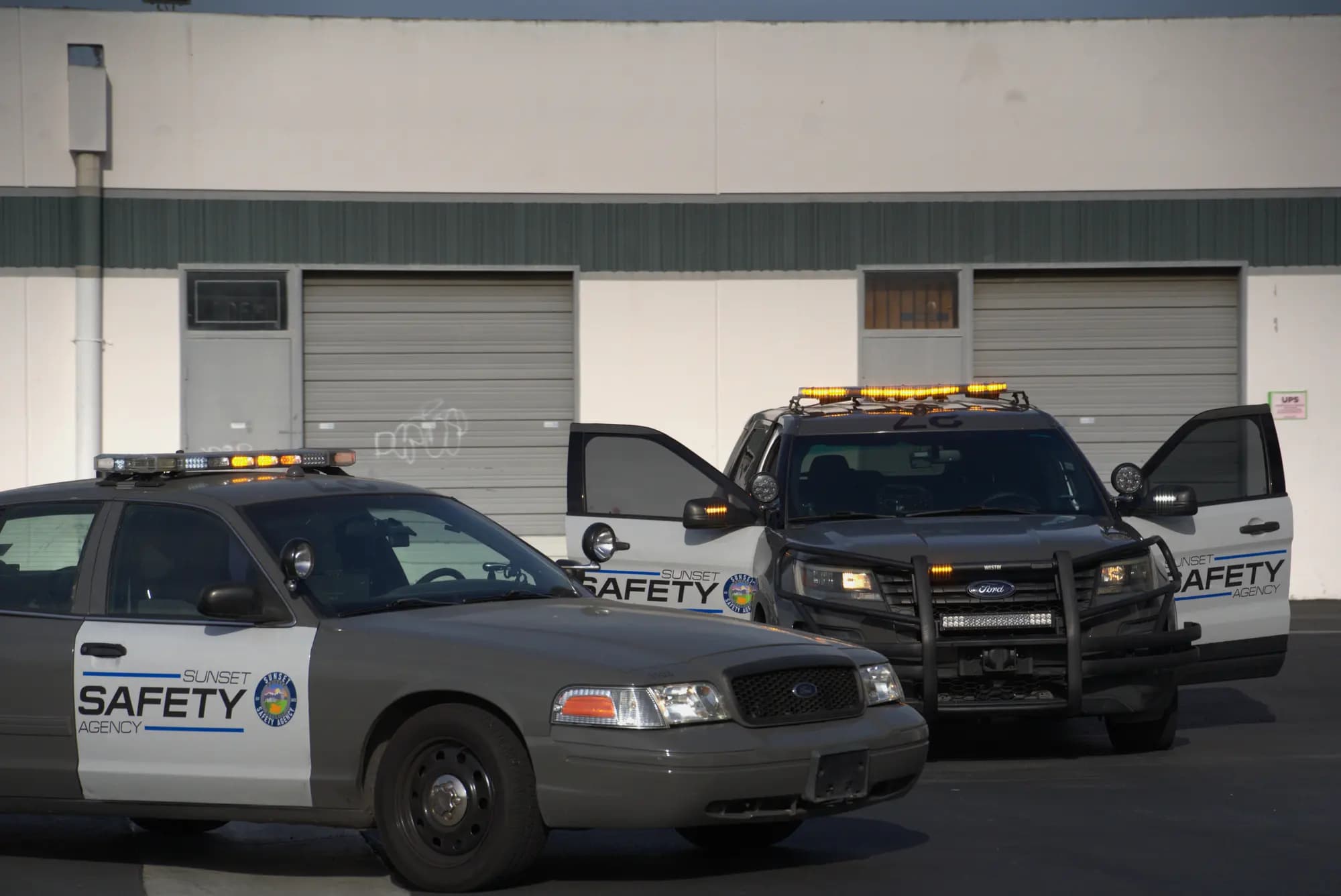 Patrol units with doors open and lightbars lit outside an industrial building
