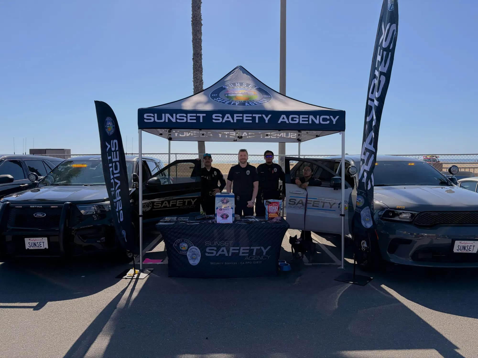 Team posed under the branded canopy flanked by patrol units at a beach event