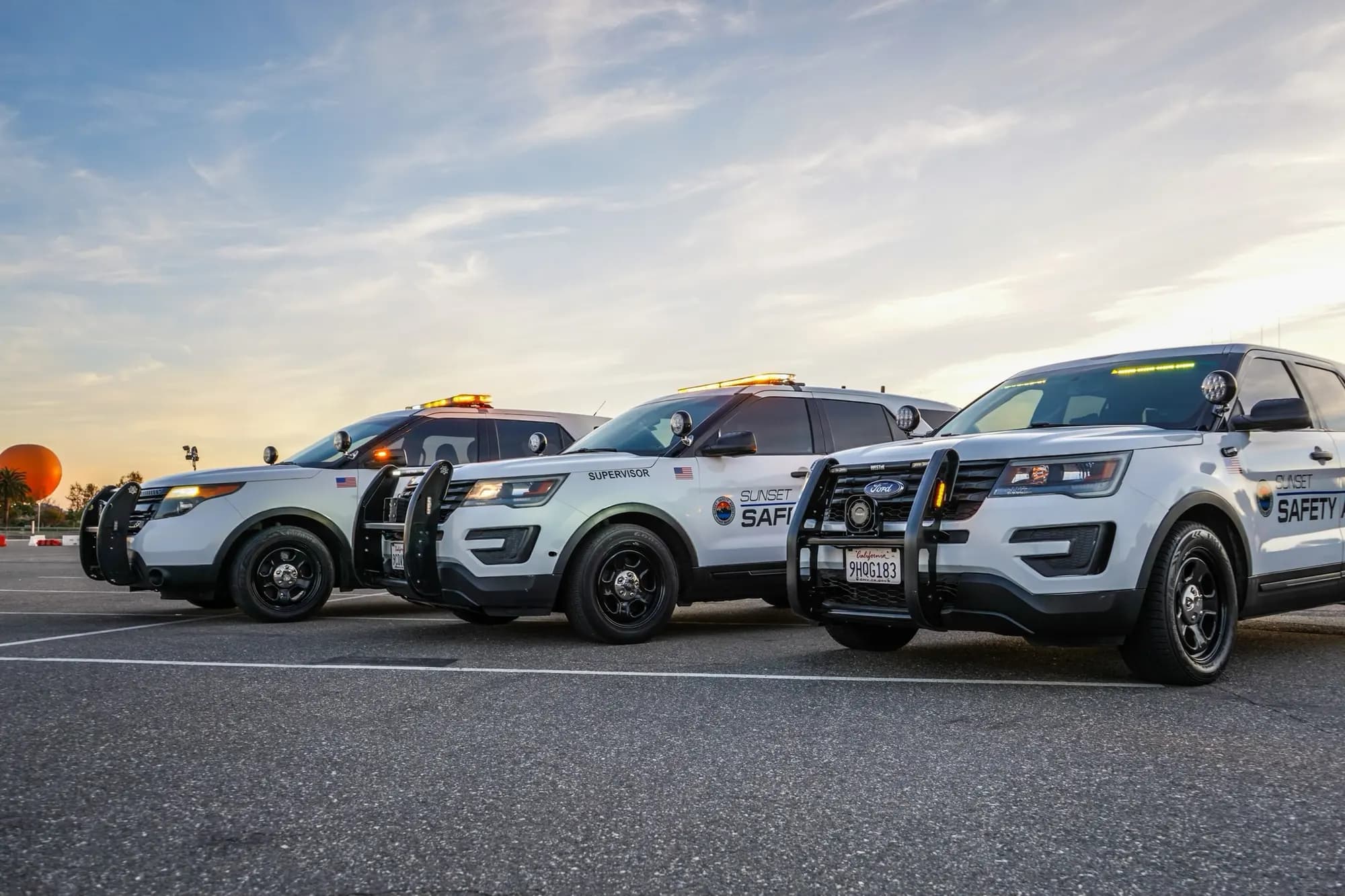 Low-angle staggered lineup of three patrol SUVs at dusk with lightbars lit