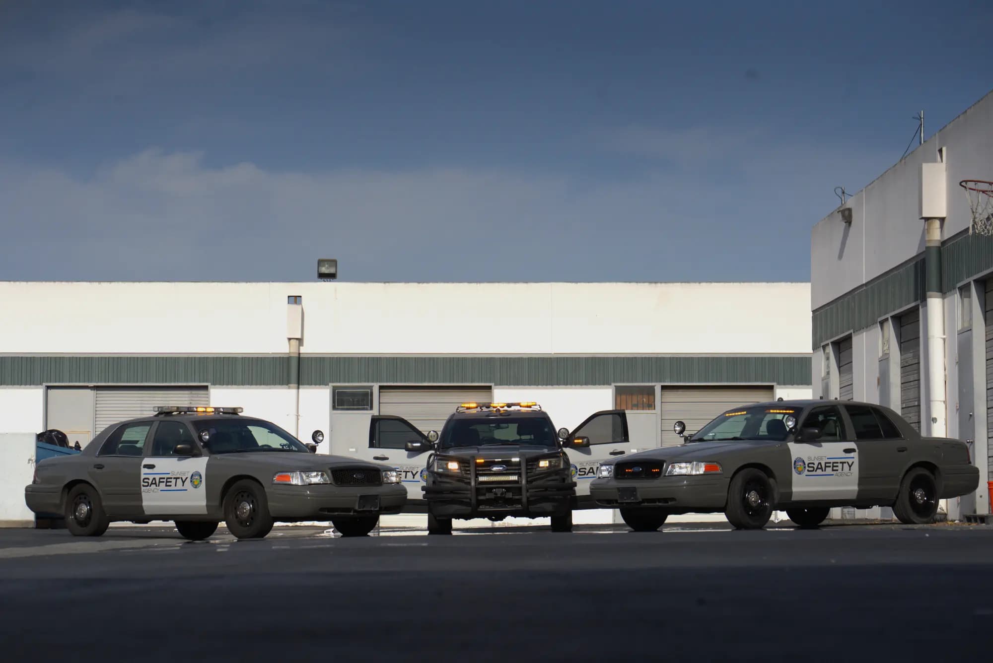 Symmetric three-vehicle patrol lineup with doors open and amber lightbars lit under a dramatic sky