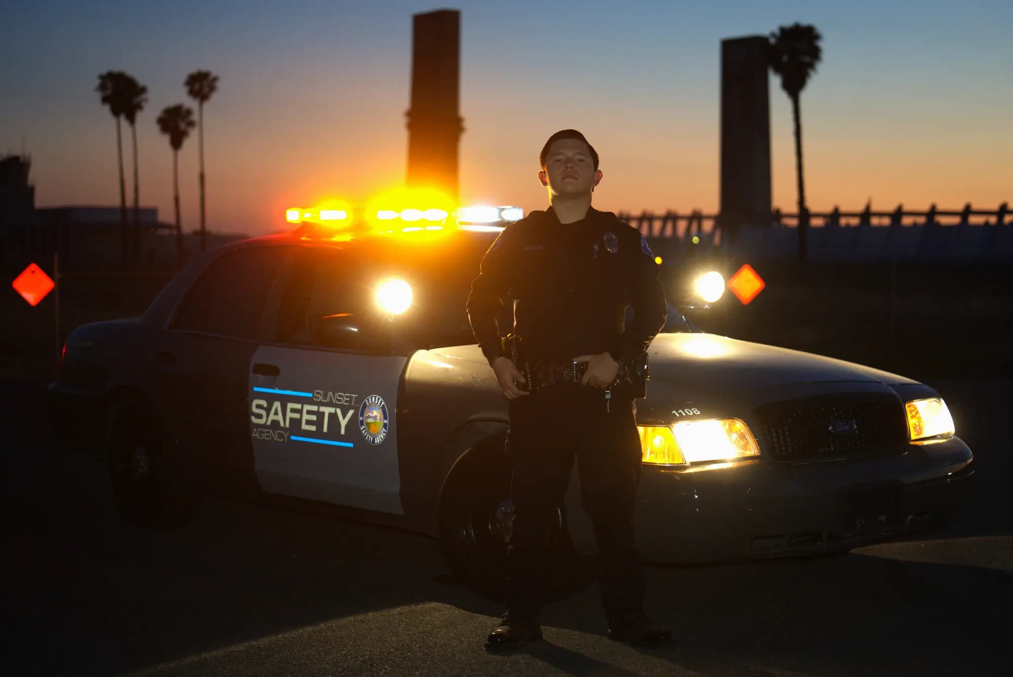 Uniformed officer standing in front of a Sunset Safety patrol car with its full lightbar lit at sunset