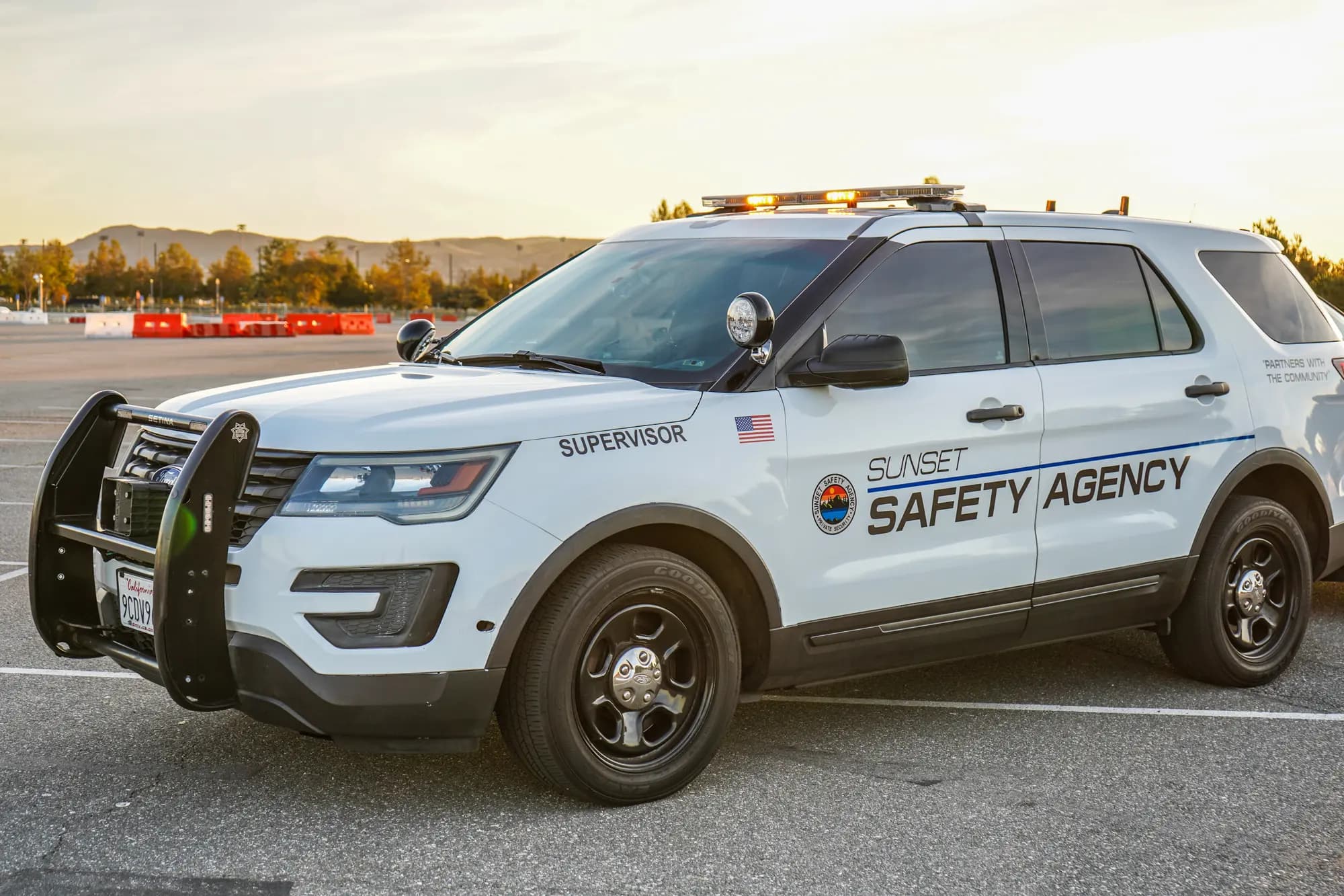 White Supervisor patrol SUV with lit amber lightbar at golden hour, hills behind