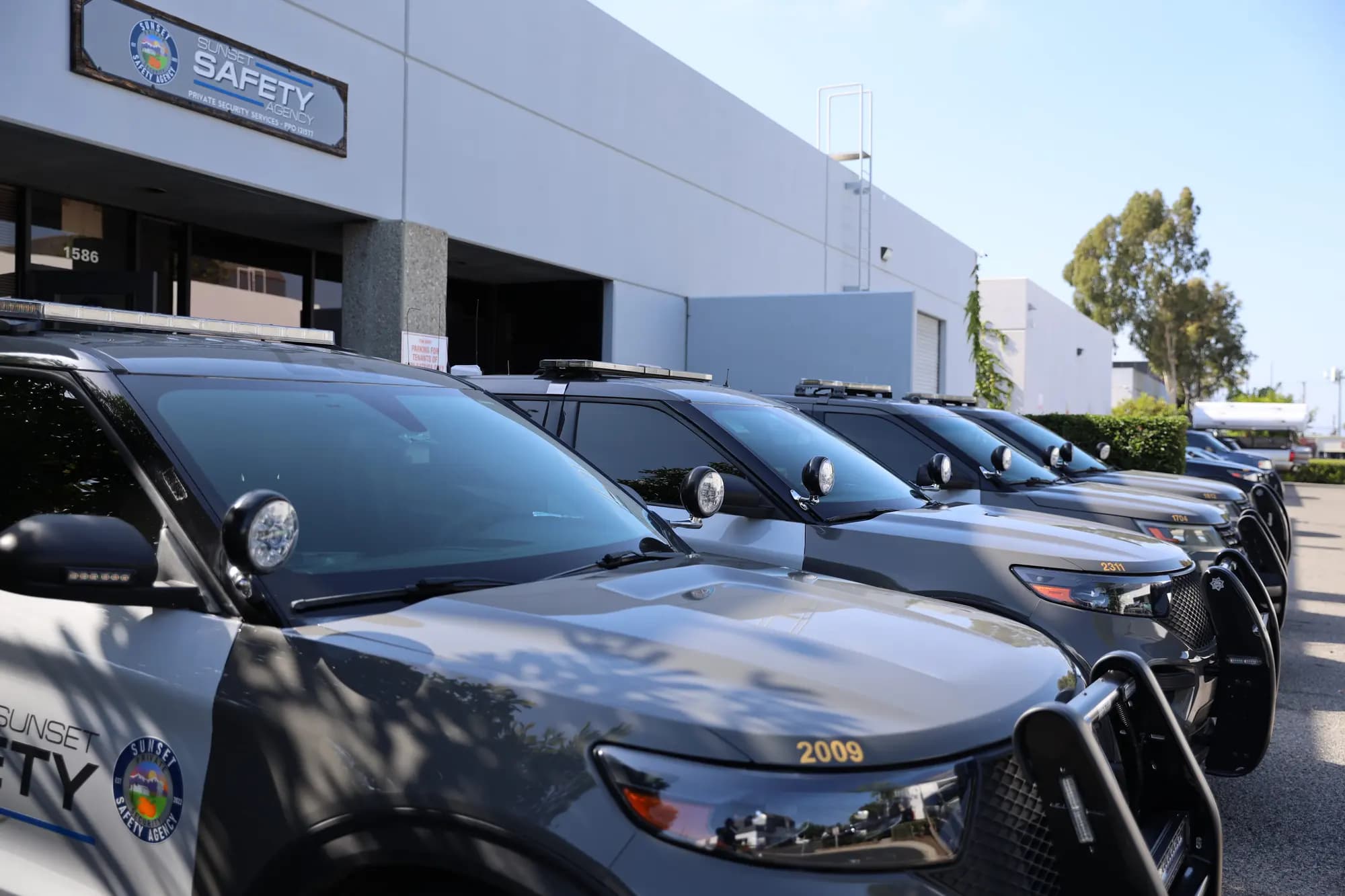 Front three-quarter view down the row of marked patrol SUVs outside headquarters