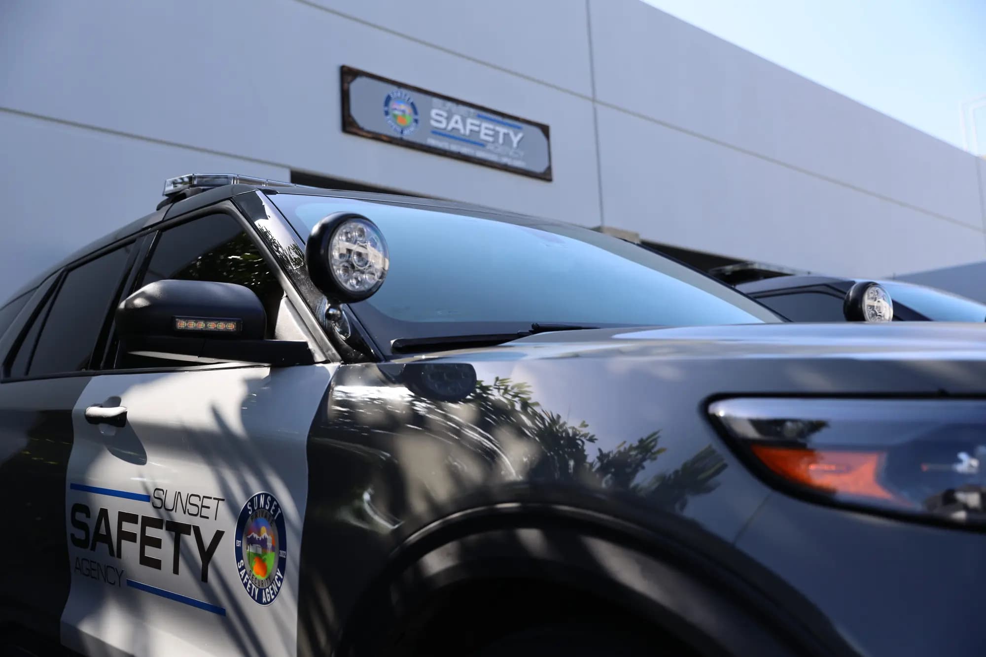 Low-angle close-up of a patrol SUV spotlight, lightbar, and door livery against blue sky