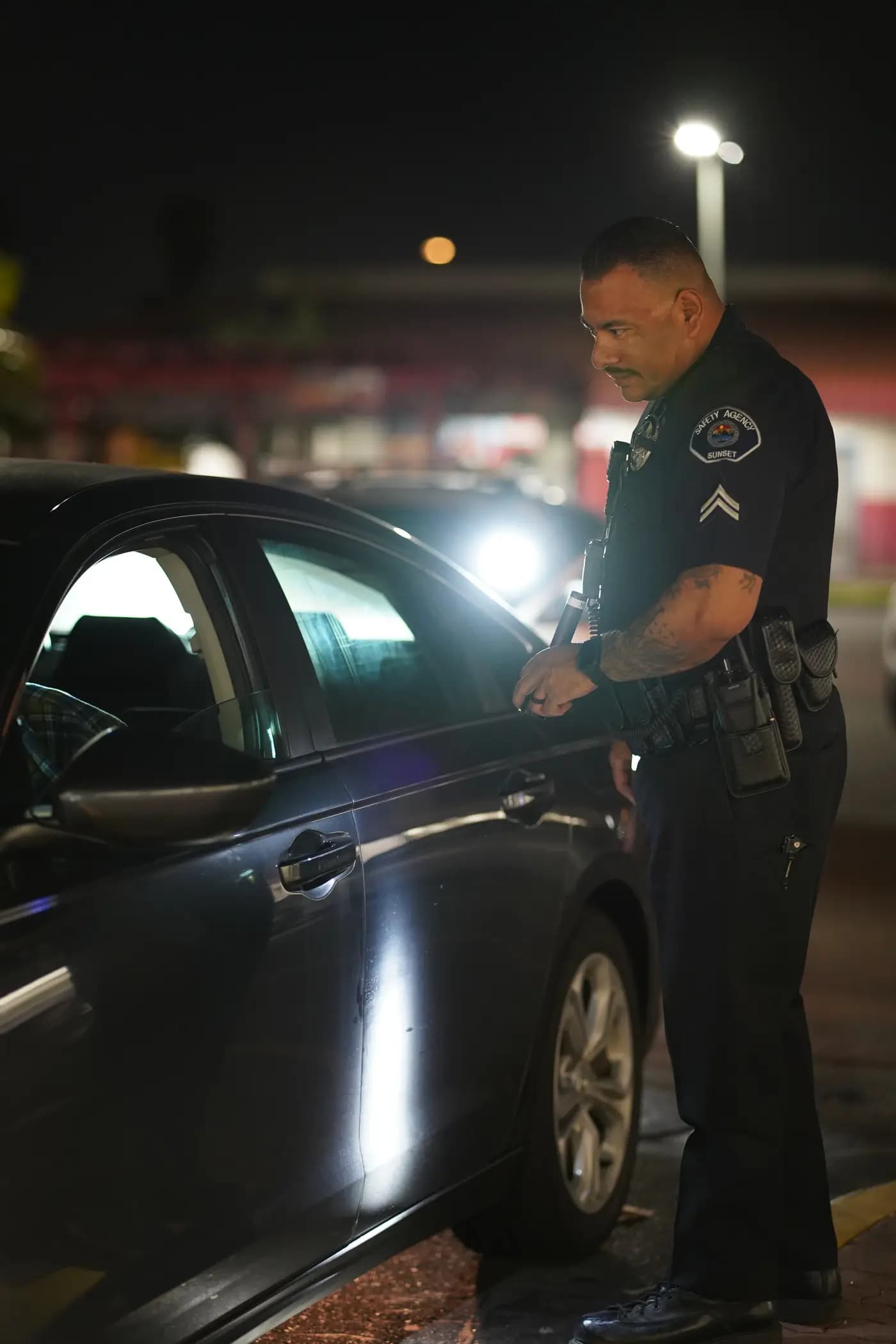 Officer inspecting a vehicle with a flashlight during a night patrol