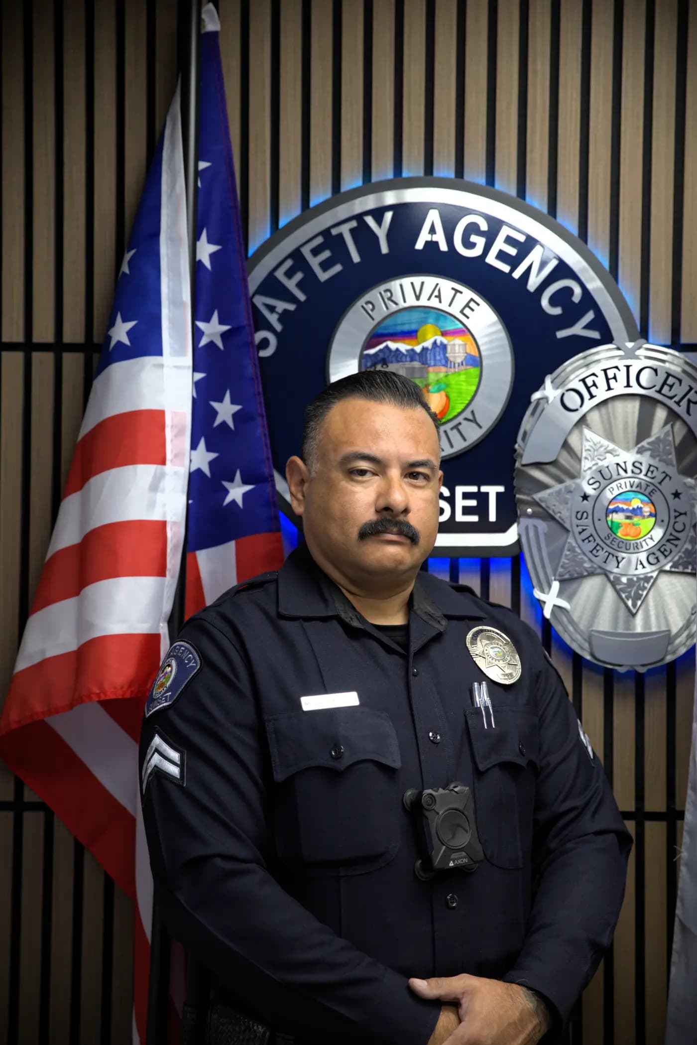 Corporal with Axon body camera at parade rest in front of the agency seal wall