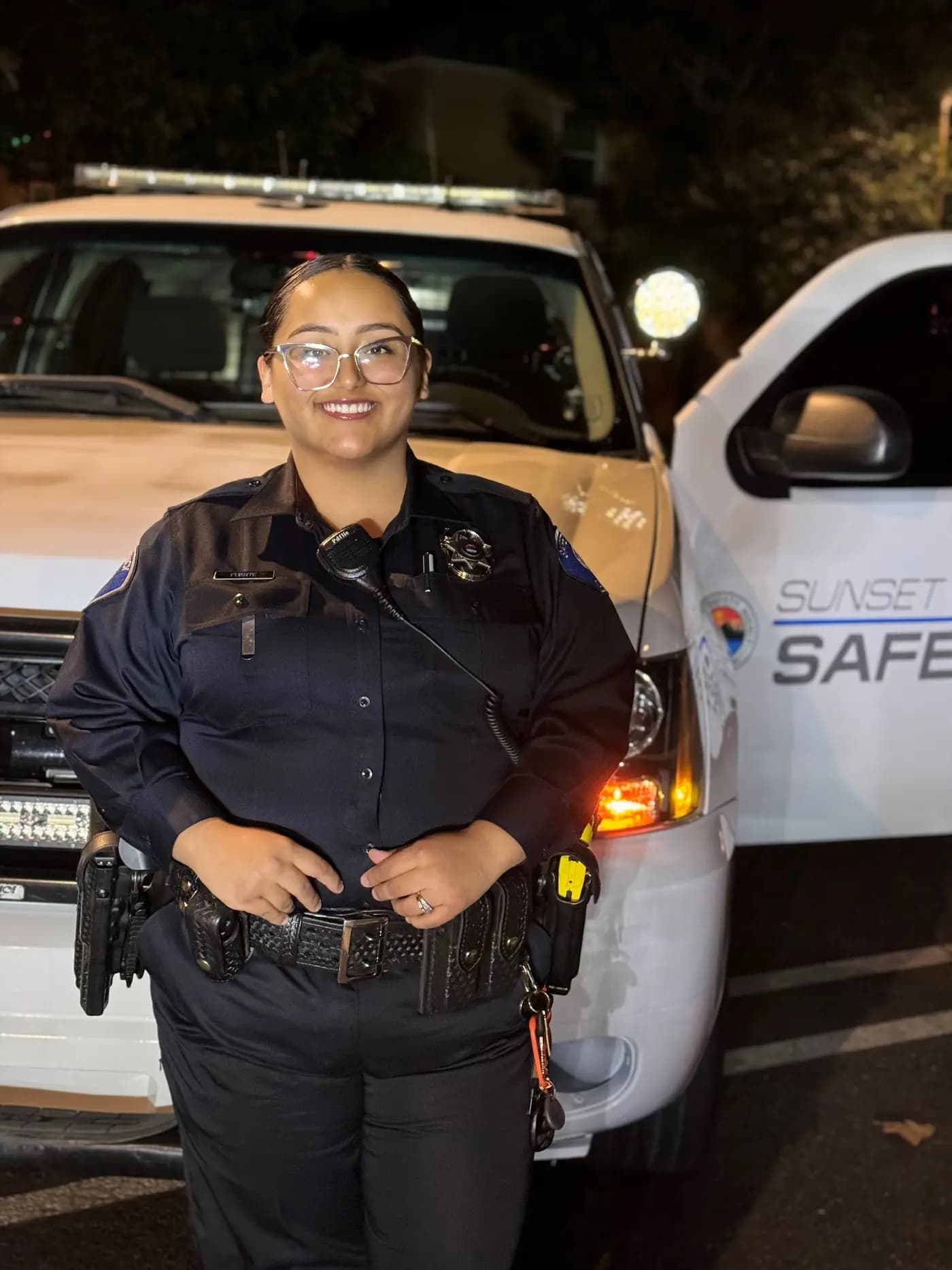 Smiling officer in navy uniform in front of a patrol Tahoe at night