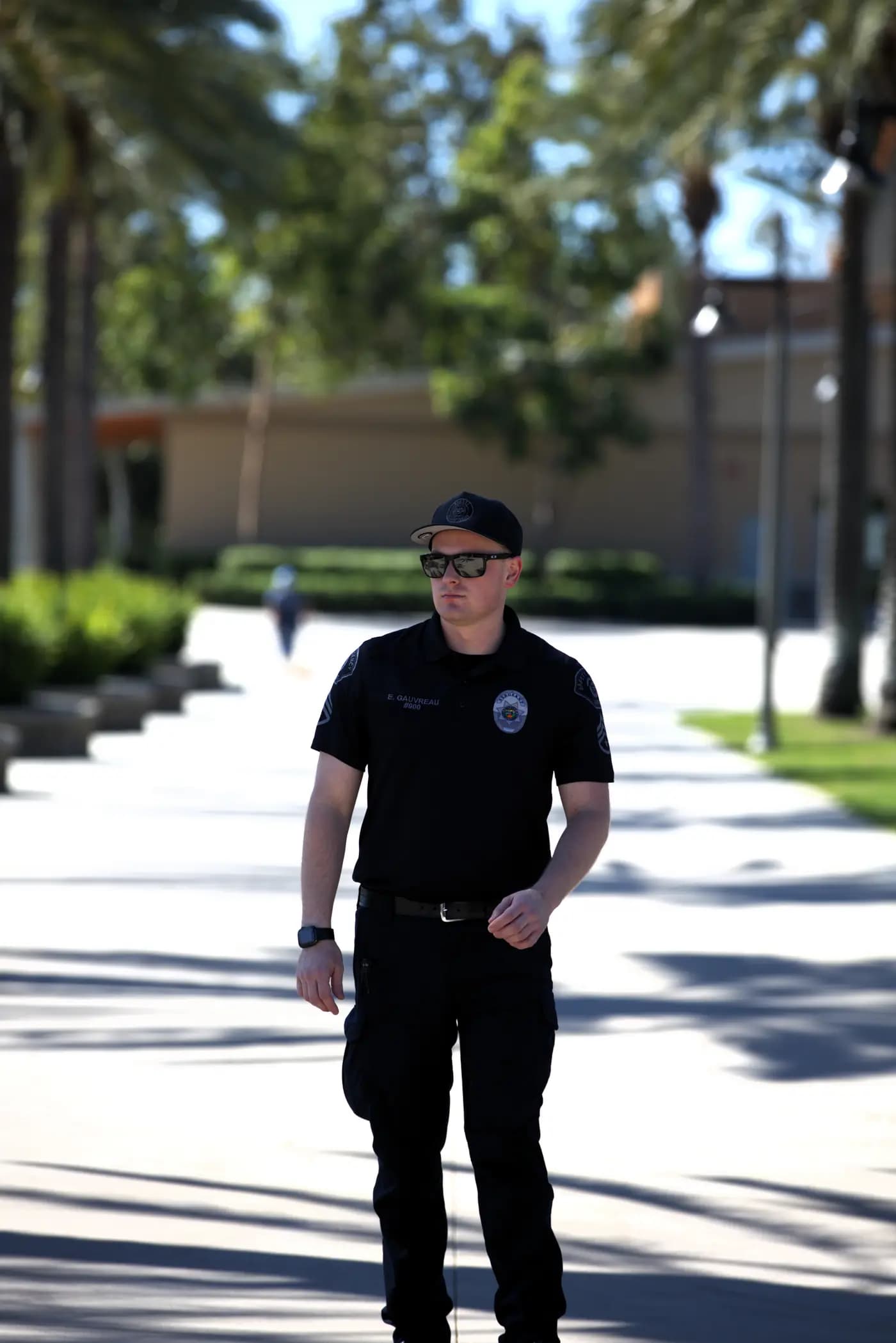 Sergeant striding a palm-lined community promenade in bright daylight