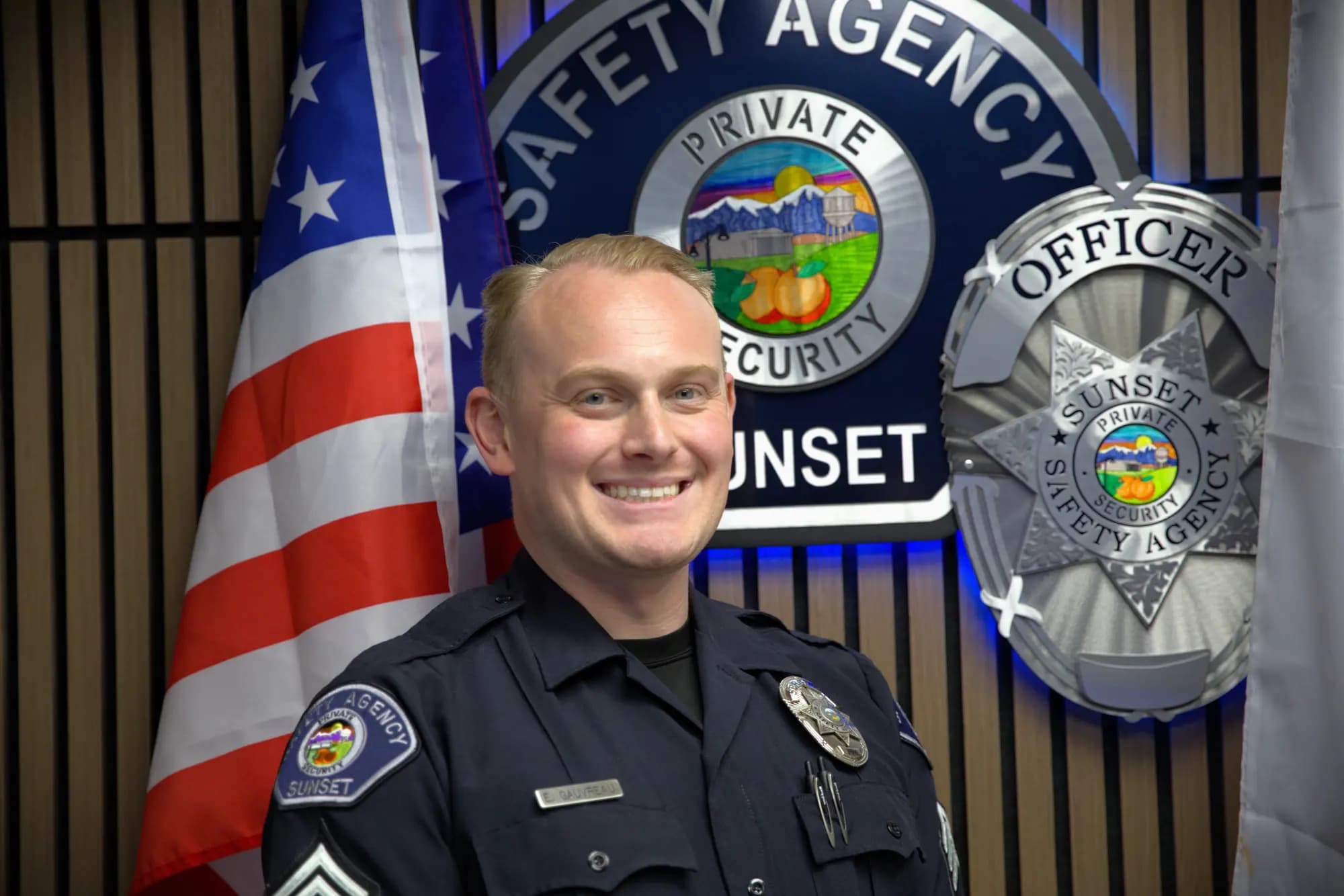 Sergeant in navy uniform in front of the backlit Sunset Safety Agency seal wall