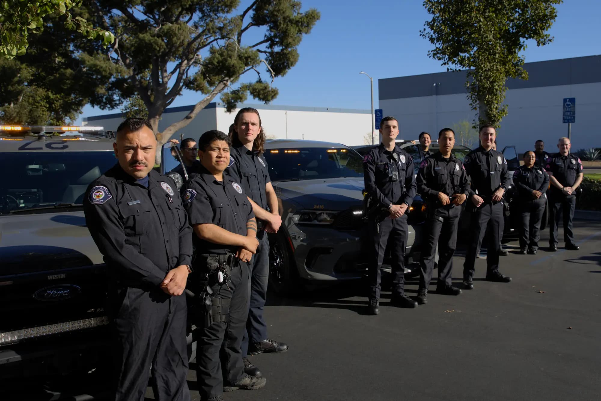 Officers standing at attention beside their marked patrol vehicles in a staggered lineup