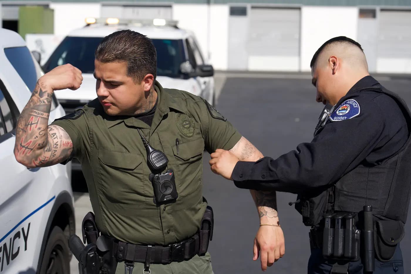 Two officers comparing tattoos between patrol vehicles in a lighthearted moment