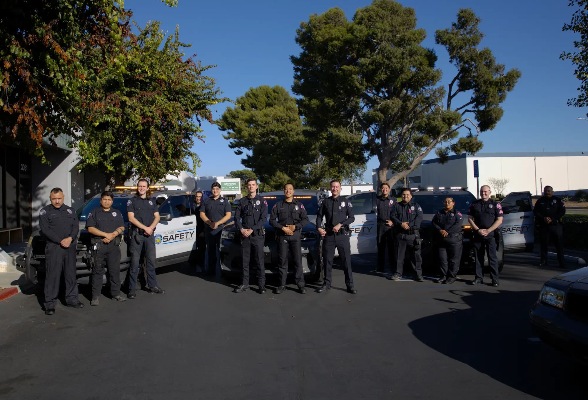 Fifteen officers spaced across a lot in front of four marked Sunset Safety units