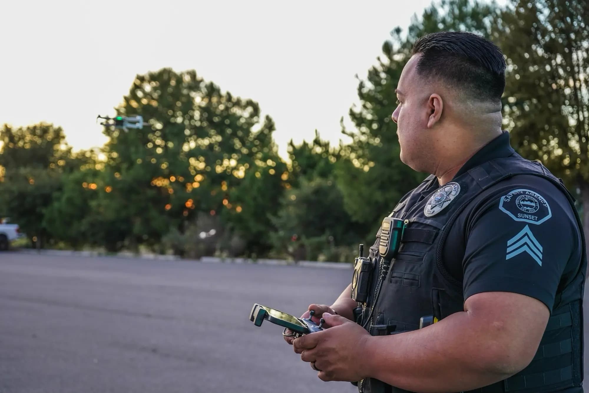 Officer in profile piloting a drone hovering over trees at dusk