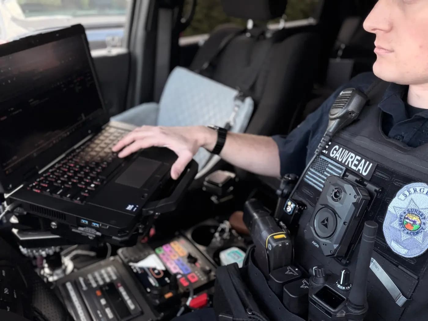 Sergeant with Axon body camera typing a report on the in-car mobile data terminal