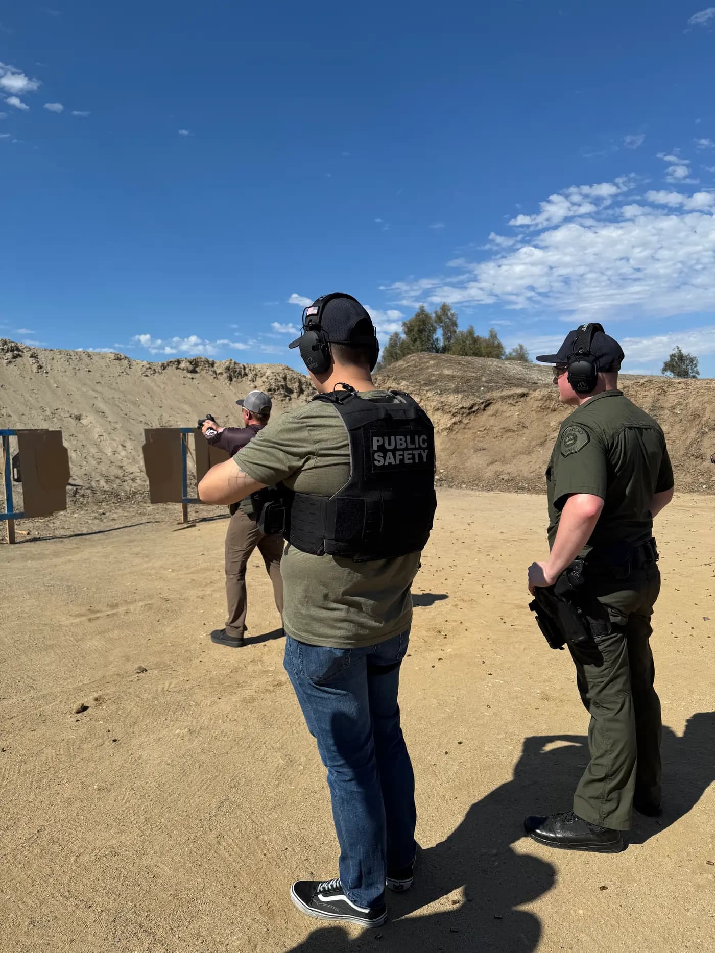 Firearms qualification training on an outdoor range with an instructor observing