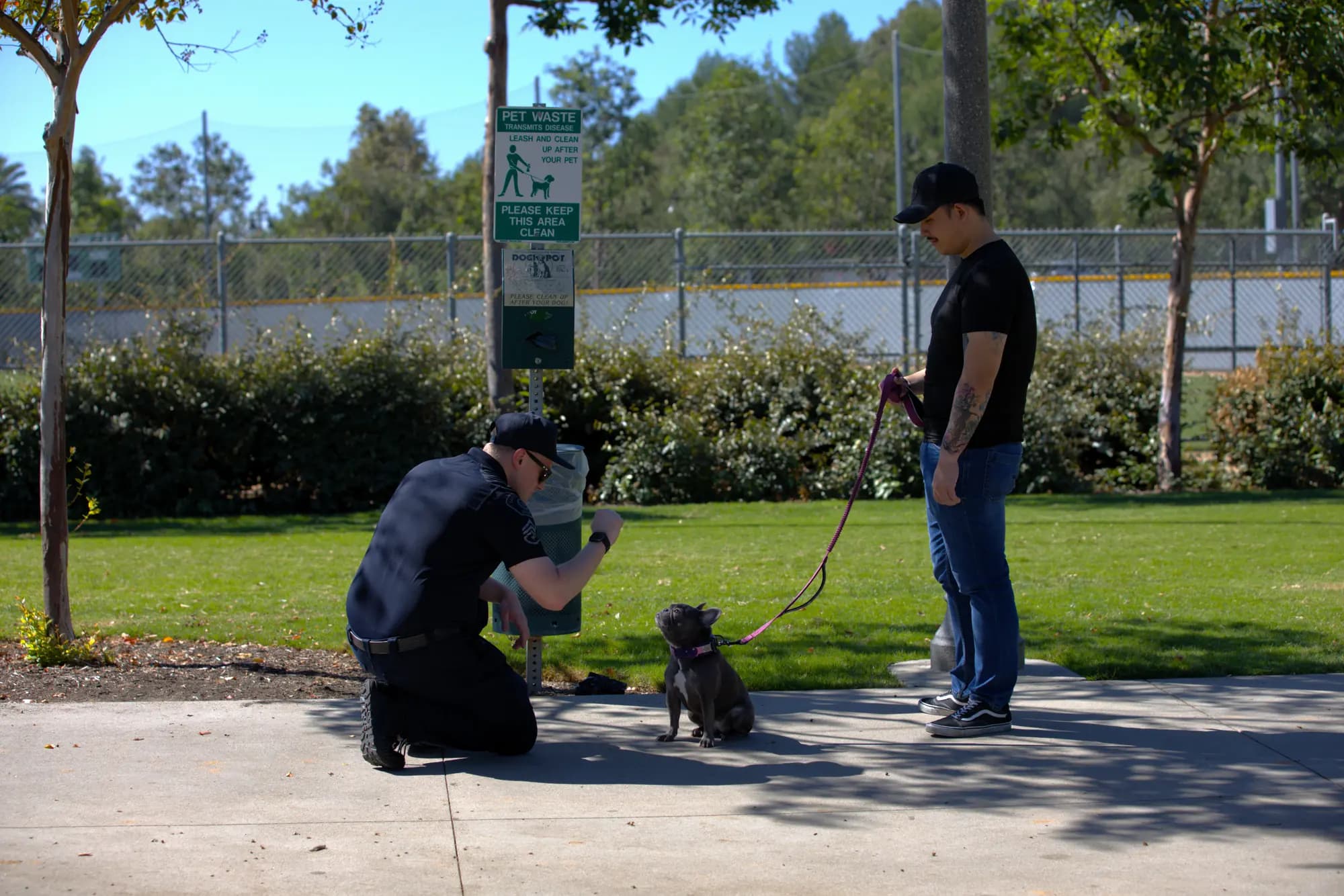 Officer kneeling to greet a resident's dog in a sunny community park