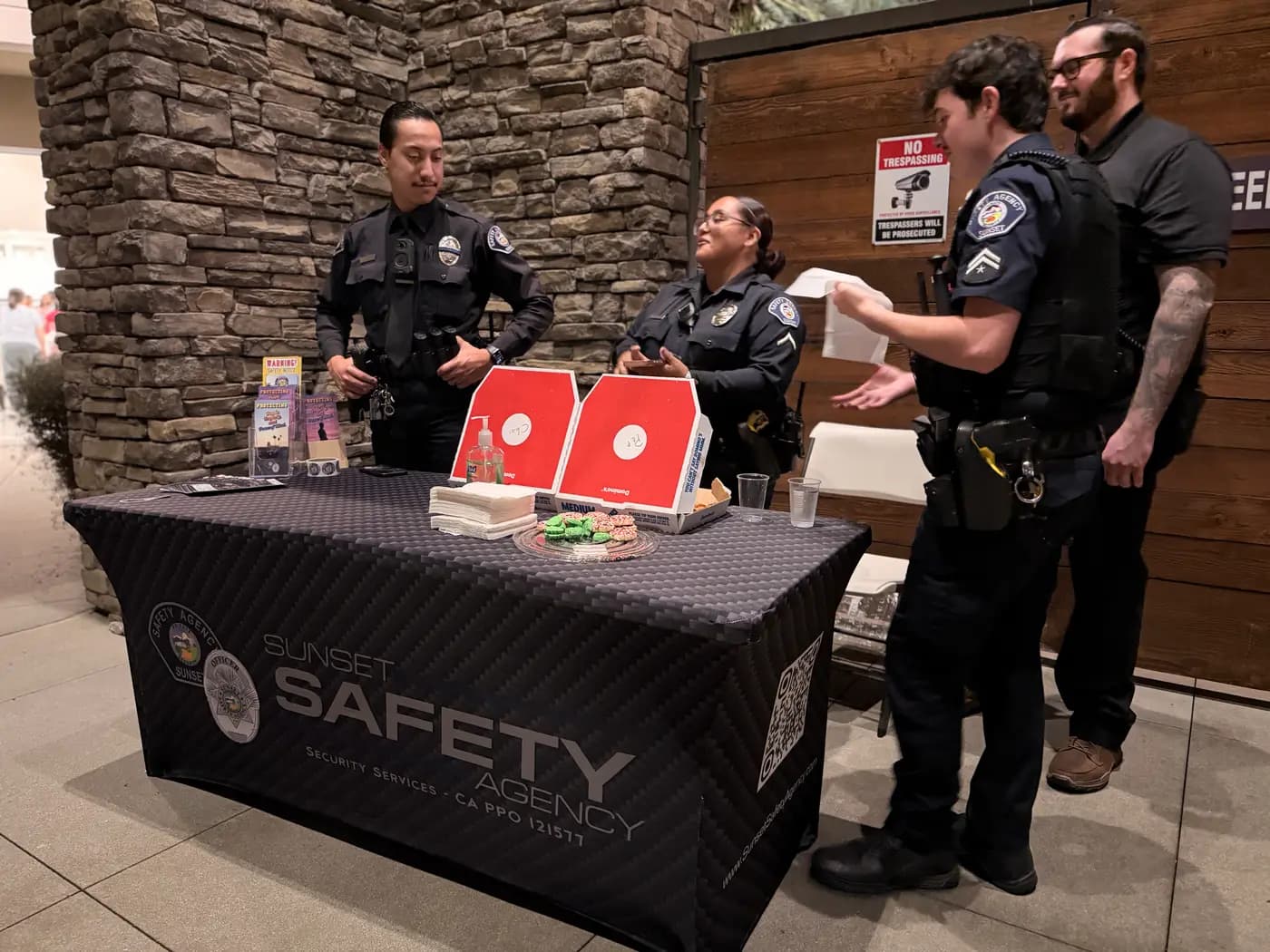 Officers laughing with residents around a branded outreach table at an evening event
