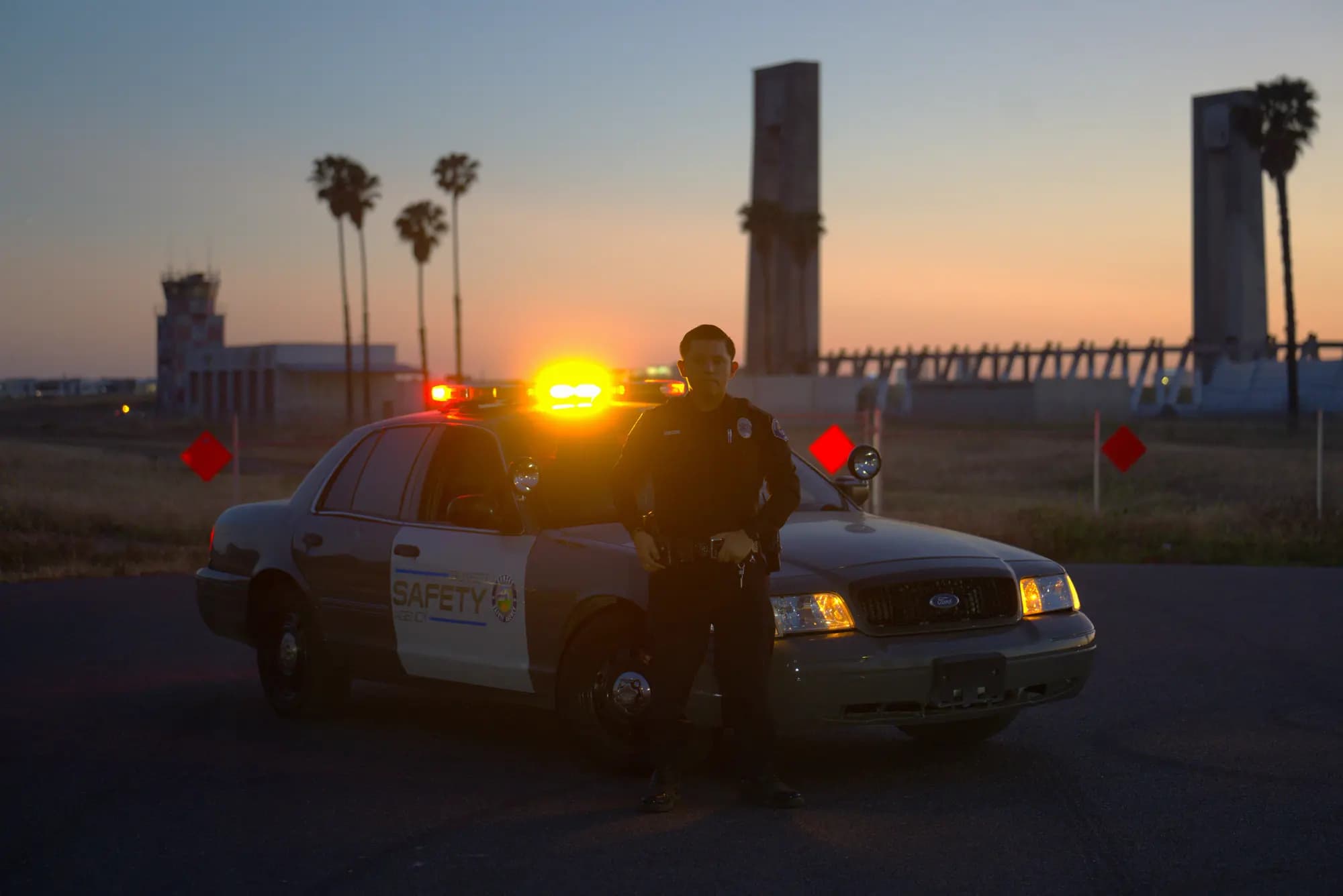 Officer leaning against a patrol car at dusk with the Great Park tower silhouetted against a peach sky