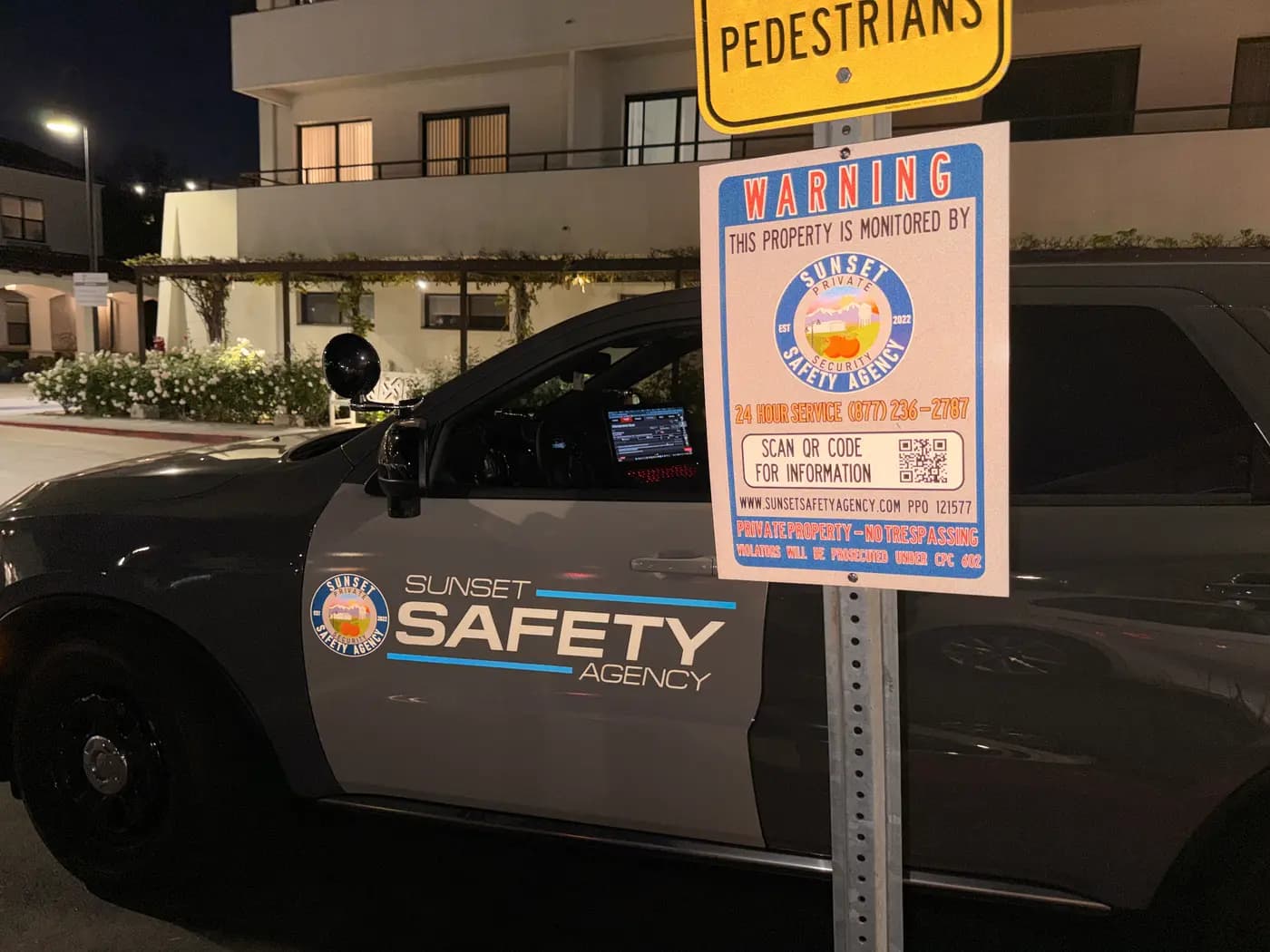 Sunset Safety Agency patrol SUV beside a property-monitored parking warning sign at night