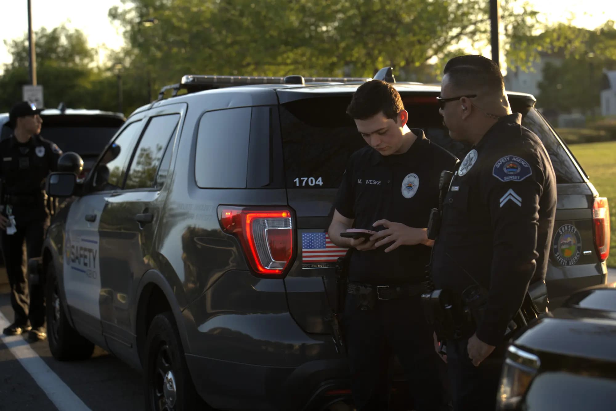 Two officers conferring over a phone at the rear of a patrol Explorer at golden hour