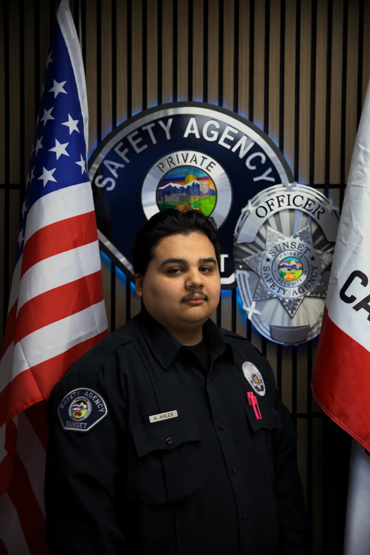 Officer roster portrait with composed expression in front of the agency shield wall