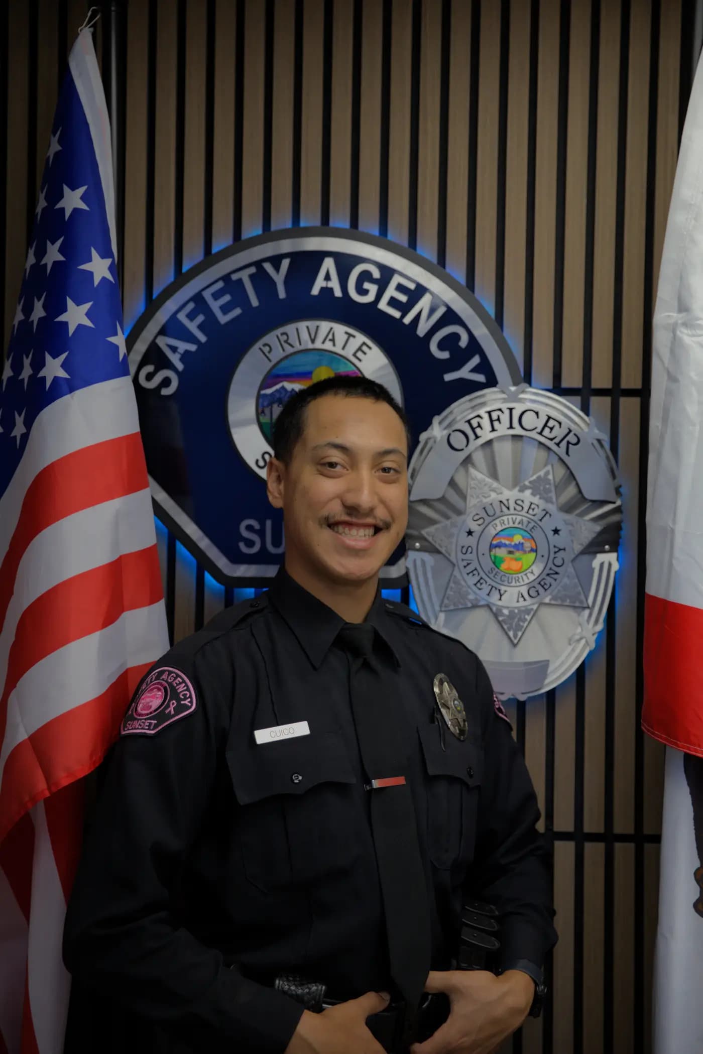 Officer smiling in Class A uniform in front of the backlit agency shield