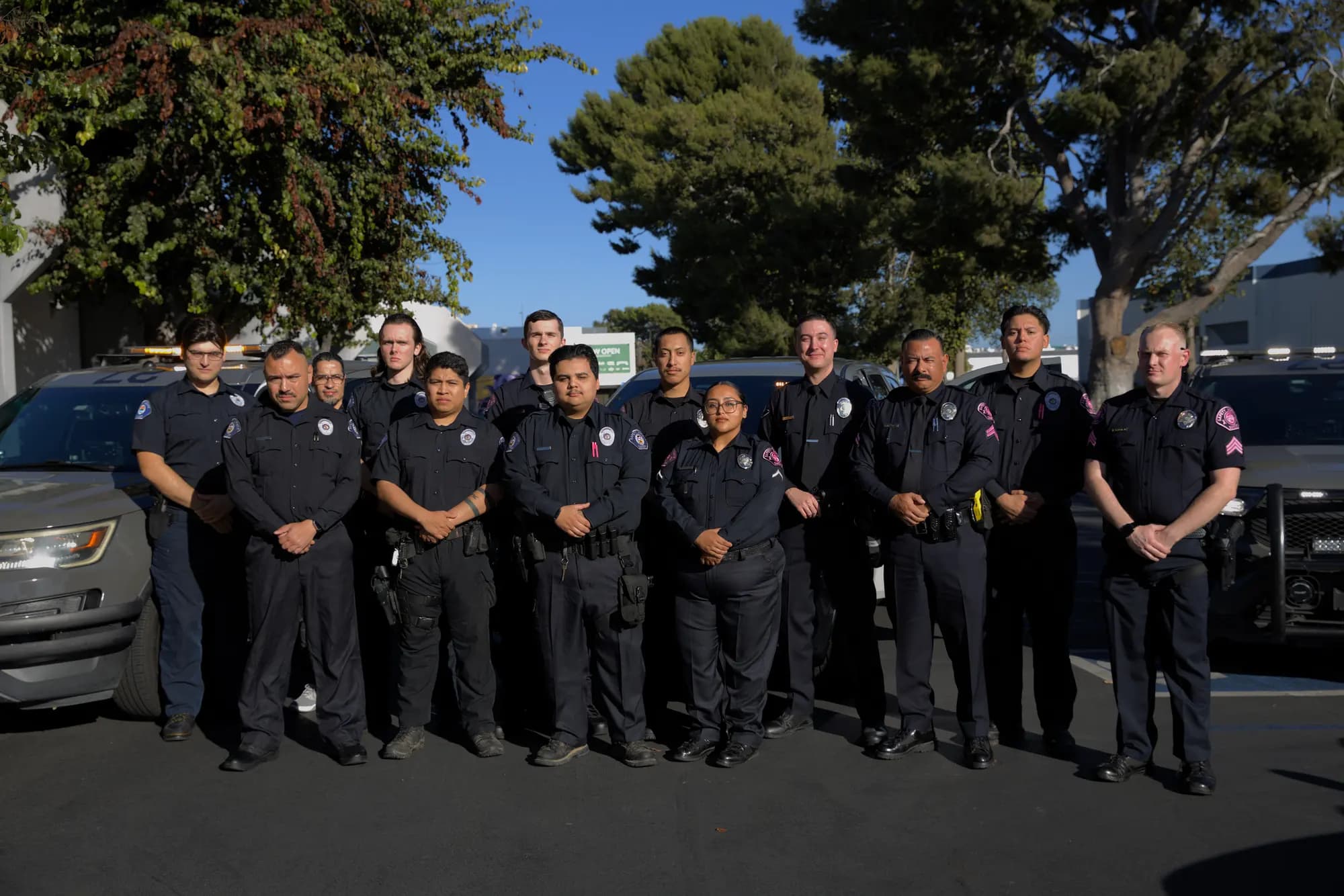 Full team group photo of fourteen uniformed officers in front of the patrol fleet